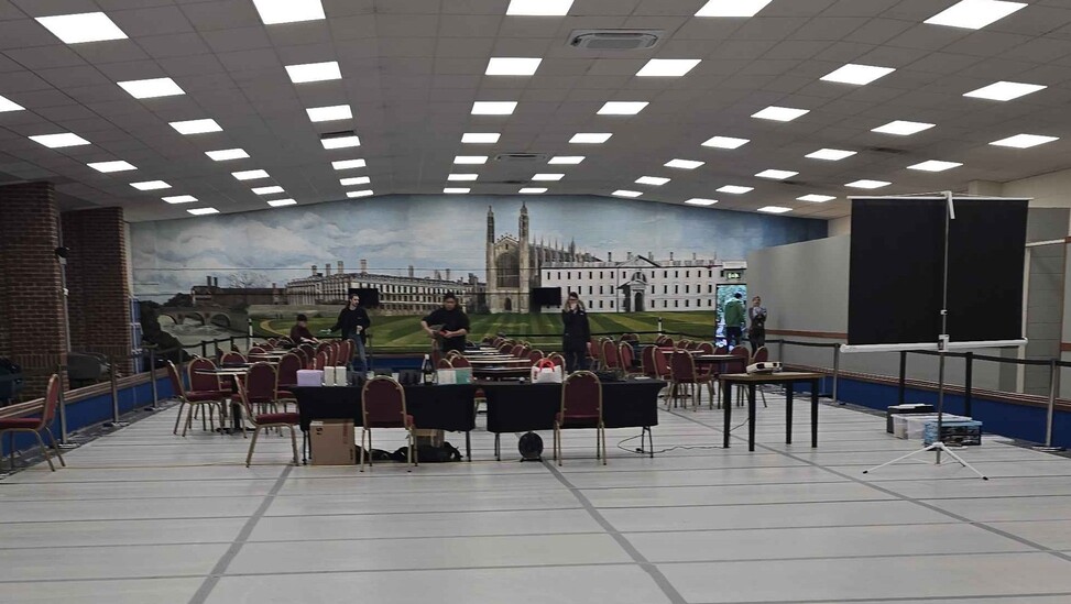 A photo of the empty tournament venue before play began: 20 tables are set up for play at the end of a covered-over bowling rink at the Chesterton Indoor Bowls Centre